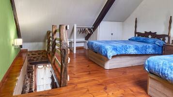 Une chambre avec un plafond en pente, un plancher en bois, un lit avec une literie bleue, une tête de lit en bois et une petite table de chevet.