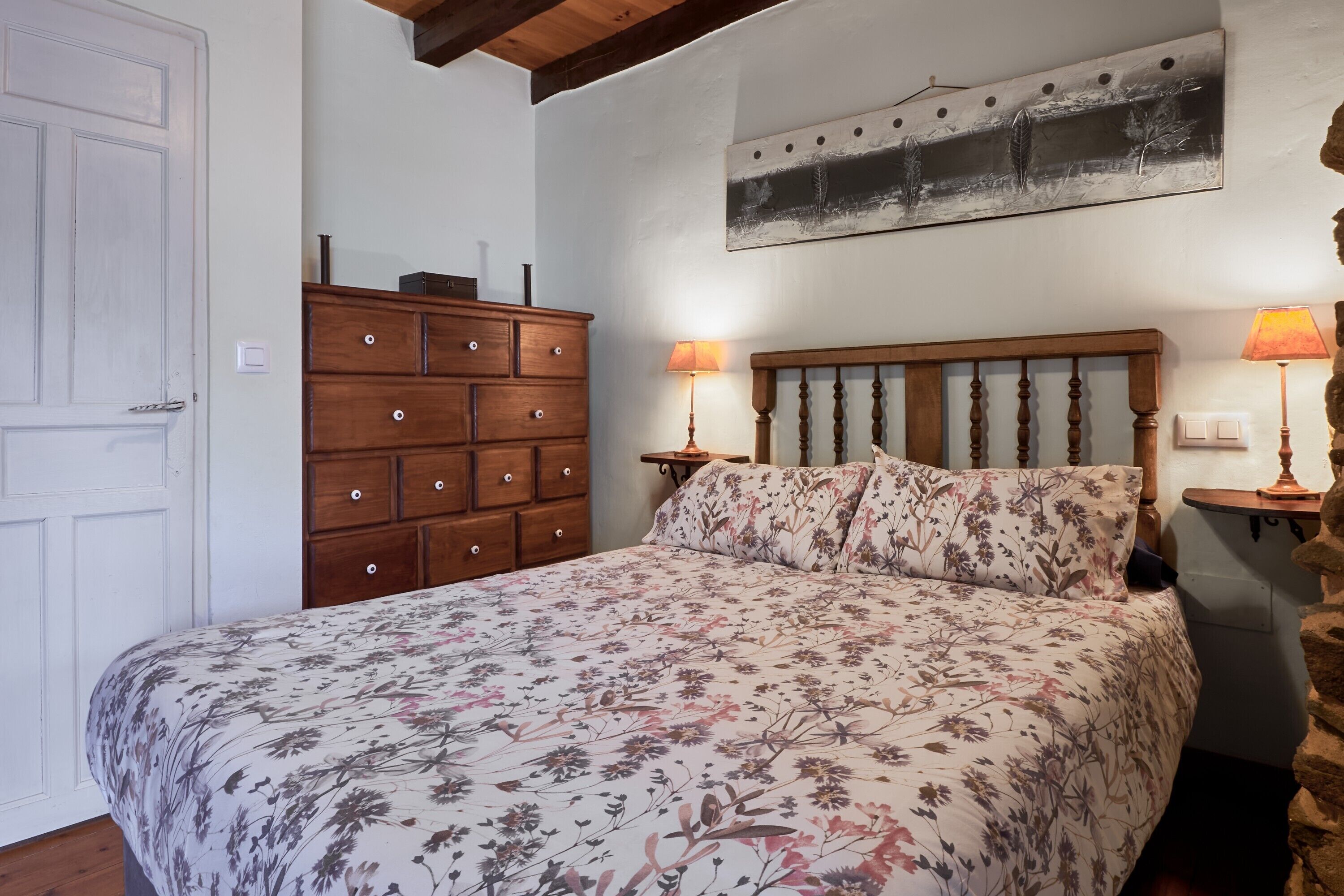 Un dormitorio con una cama de madera, ropa de cama floral, un tocador y dos lámparas de noche.