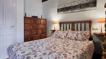 Un dormitorio con una cama de madera, ropa de cama floral, un tocador y dos lámparas de noche.