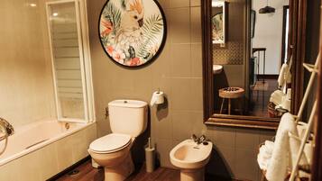 Une salle de bain équipée de toilettes, d’un bidet, d’une baignoire et d’un grand miroir.