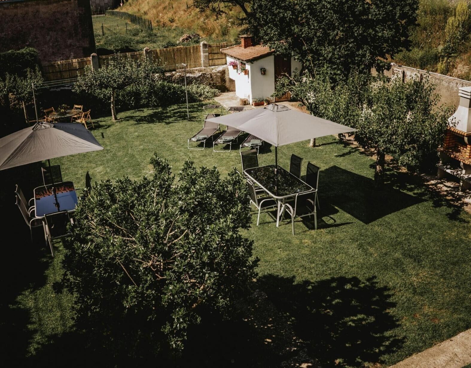 Un patio con césped, una mesa y sillas, un pequeño edificio blanco y una valla de madera.