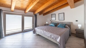 Une chambre à coucher avec un grand lit, des poutres apparentes en bois au plafond, une table de chevet et une fenêtre offrant une belle vue.