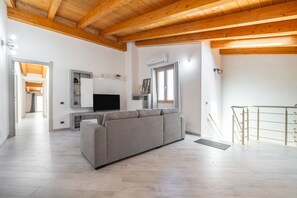 A modern living room with a grey sofa, wooden ceiling beams, a flat-screen TV, and a staircase with a metal railing. - Holiday Home 'Sea View' with Sea View, Wi-Fi and Air Conditioning (Portoscuso)