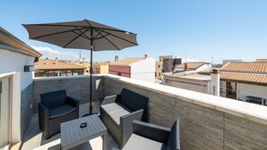 Une terrasse sur le toit, aménagée avec des meubles en osier, une table et un grand parasol.
