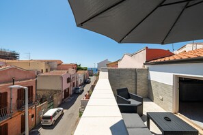 A residential street with a row of houses, a parked car, and a covered outdoor seating area with a table and chairs. - Holiday Home 'Sea View' with Sea View, Wi-Fi and Air Conditioning (Portoscuso)