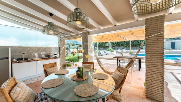 An outdoor dining area with wicker furniture, a glass table, and hanging lights. - Villa 'Tranquila El Retiro' with Private Pool, Wi-Fi and Air Conditioning (Málaga)