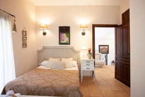 Une chambre d’hôtel avec un lit, des tables de chevet, des lampes fixées au mur, un tableau et une porte donnant sur une autre pièce.
