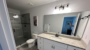 Une salle de bain moderne avec une douche à parois de verre, des toilettes, un lavabo avec un grand miroir et des meubles blancs.