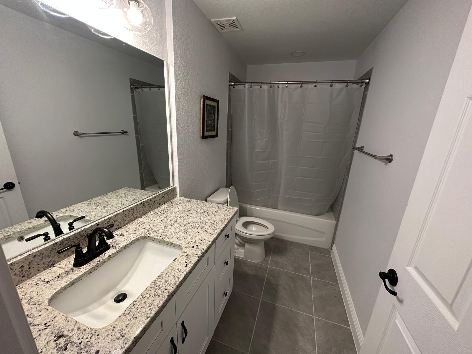 A bathroom with a granite countertop sink, a toilet, and a shower with a curtain.