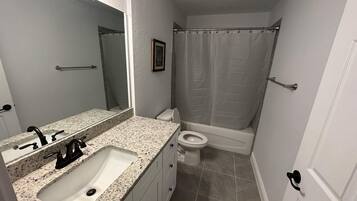 A bathroom with a granite countertop sink, a toilet, and a shower with a curtain.