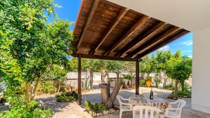 En udendørs terrasse med et træbeklædt pergola, et bord med stole og krukker med planter.