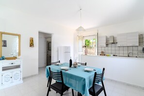 A dining area with a table set for four, a white cabinet with a mirror, and a window with a view of greenery. - Holiday Home 'Villa Ottavia' with Private Terrace, Wi-Fi and Air Conditioning (Torre Lapillo)