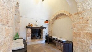 Ein Zimmer mit Steinwänden, einem Kamin, einer Bank und einem Regal mit Dekorationen.
