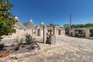 Un patio con edificios de piedra, un pérgola y asientos al aire libre.