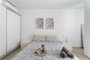 A minimalist bedroom with a bed, bedside tables, and a wall-mounted air conditioner.