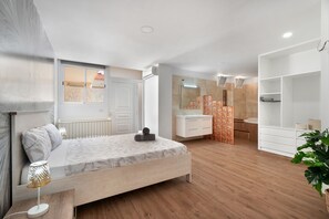 A modern bedroom with a wooden bed, a bedside lamp, a bathroom with a shower, and a large mirror.
