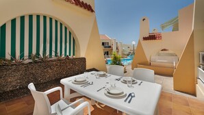 A dining area with a table set for four, outdoor seating, a pool, and a view of the resort buildings. - Vacation Apartment 'Beach Holidays' with Shared Pool, Wi-Fi and Air Conditioning (Adeje)