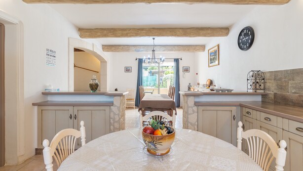 A dining area with a round table, chairs, a bowl of fruit, a chandelier, and a view through an open doorway. - Holiday Home 'Mas Provençal' with Private Pool, Wi-Fi and Air Conditioning (Saint-Rémy-de-Provence)