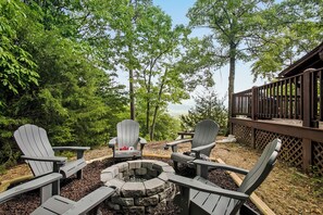 Eine Terrasse mit Adirondack-Stühlen und einem Feuerkorb, umgeben von Bäumen.