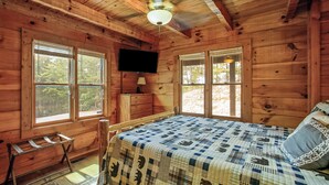 A wooden cabin room with a bed, a television, and two windows. - NEW!! Mountain Views! Quiet Escape w/ Fire Pit, Hot Tub, Front Porch Sitting (Sevierville)