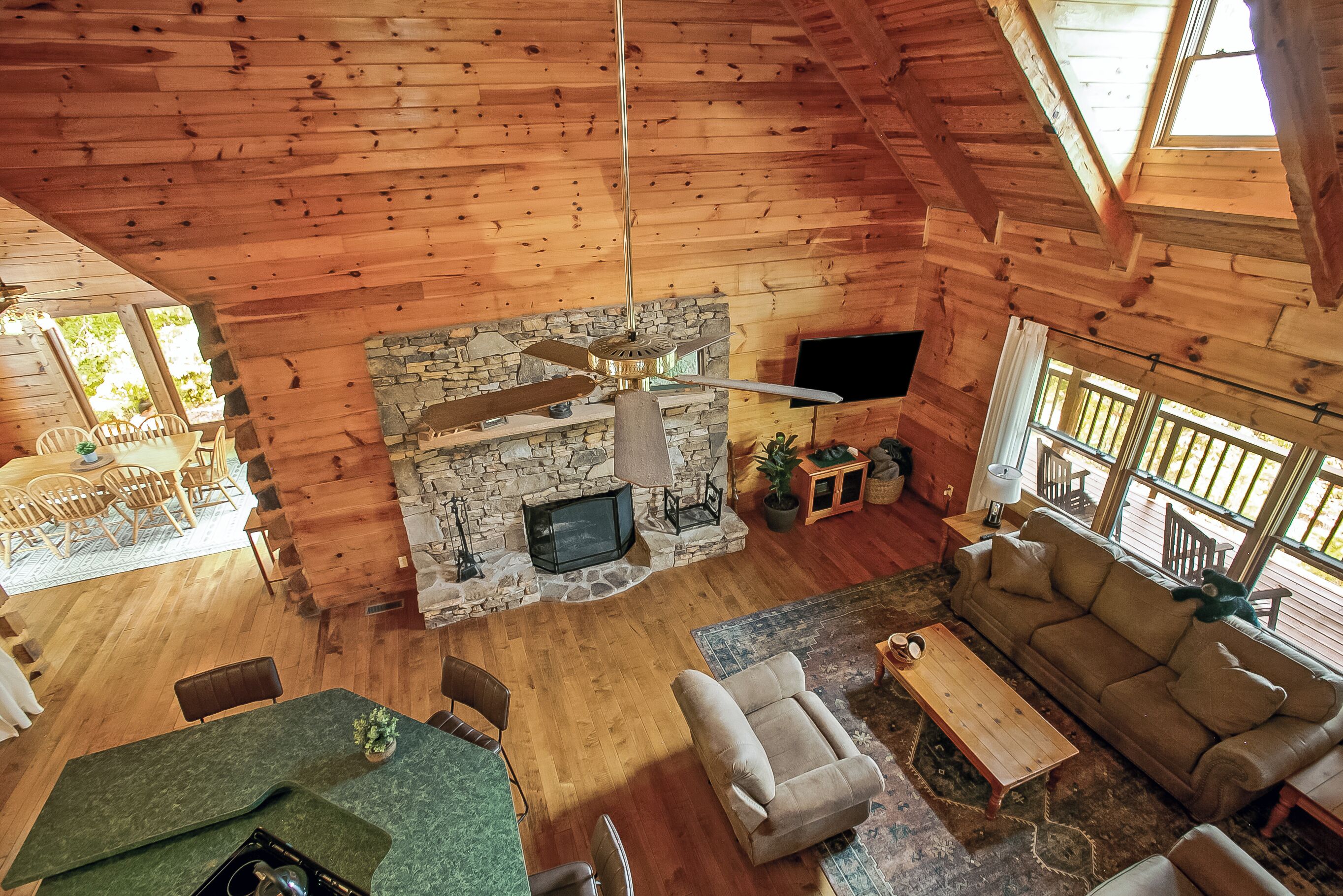 A spacious living area with a stone fireplace, wooden ceiling, and a large window.