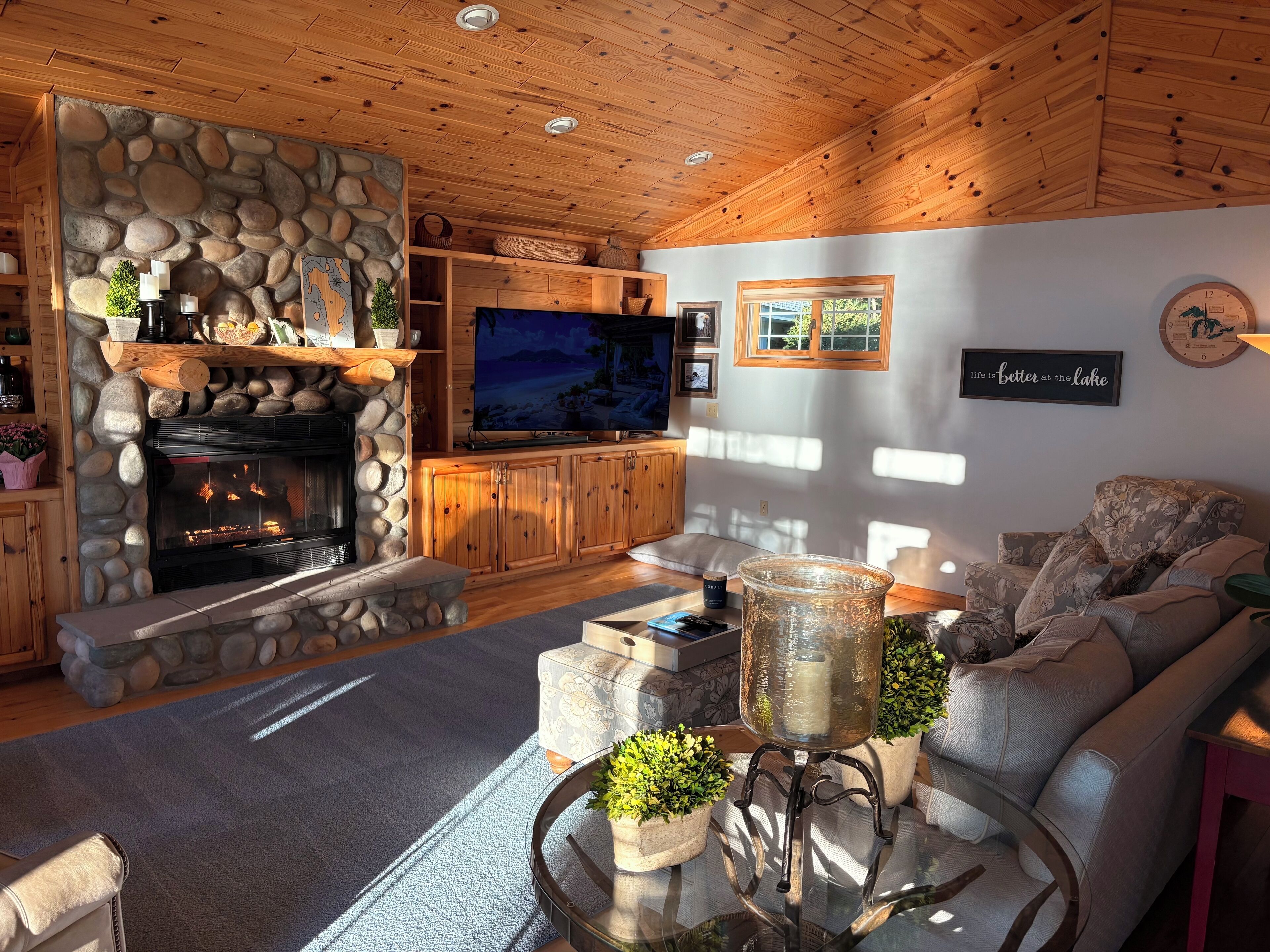 Una sala de estar acogedora con chimenea de piedra, techo de madera y televisor.