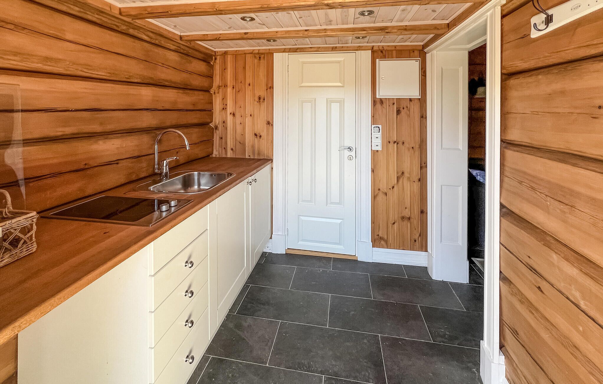 Una cocina compacta con paredes de madera, una puerta blanca y piso de baldosas.