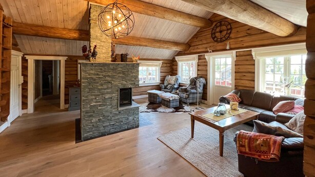 A log cabin interior with a stone fireplace, wooden ceiling beams, and a cozy seating area with a sofa and armchairs. - Gorgeous home in øyer with sauna (Øyer)