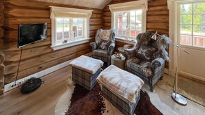 A cozy cabin interior with wooden walls, plaid furniture, a television, and a large window providing a view of the outside. - Gorgeous home in øyer with sauna (Øyer)