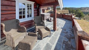 A wooden cabin with wicker furniture on a stone patio overlooking a forested landscape. - Gorgeous home in øyer with sauna (Øyer)