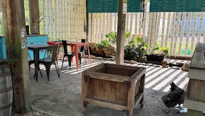 An outdoor patio area with a wooden table and chairs, a wooden planter, and a chicken pecking at the ground.