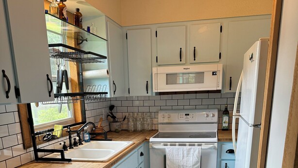 A kitchen with light blue cabinets, a white stove, and a microwave.
