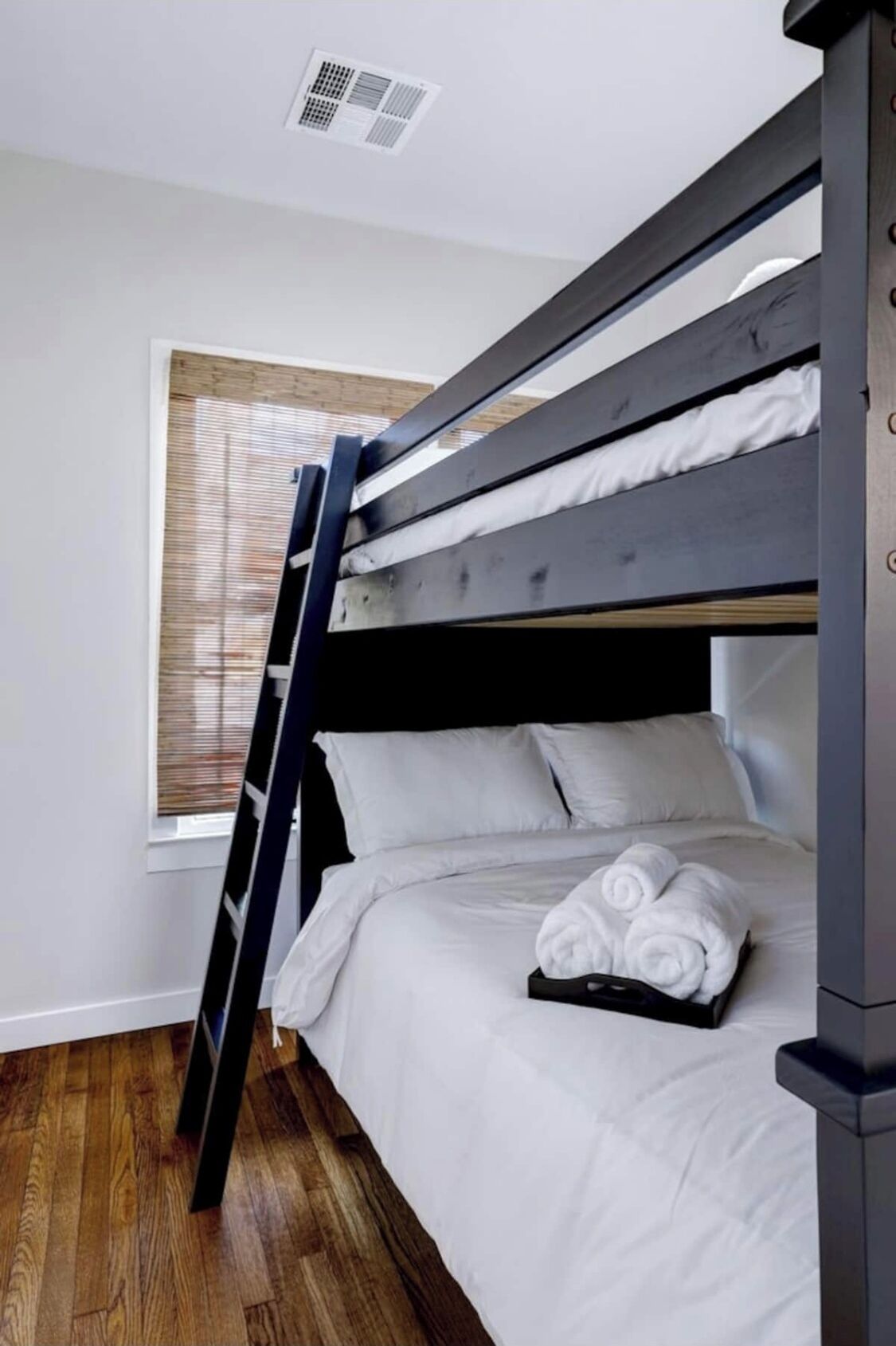 A bunk bed with white bedding and a rolled towel on the lower bunk.