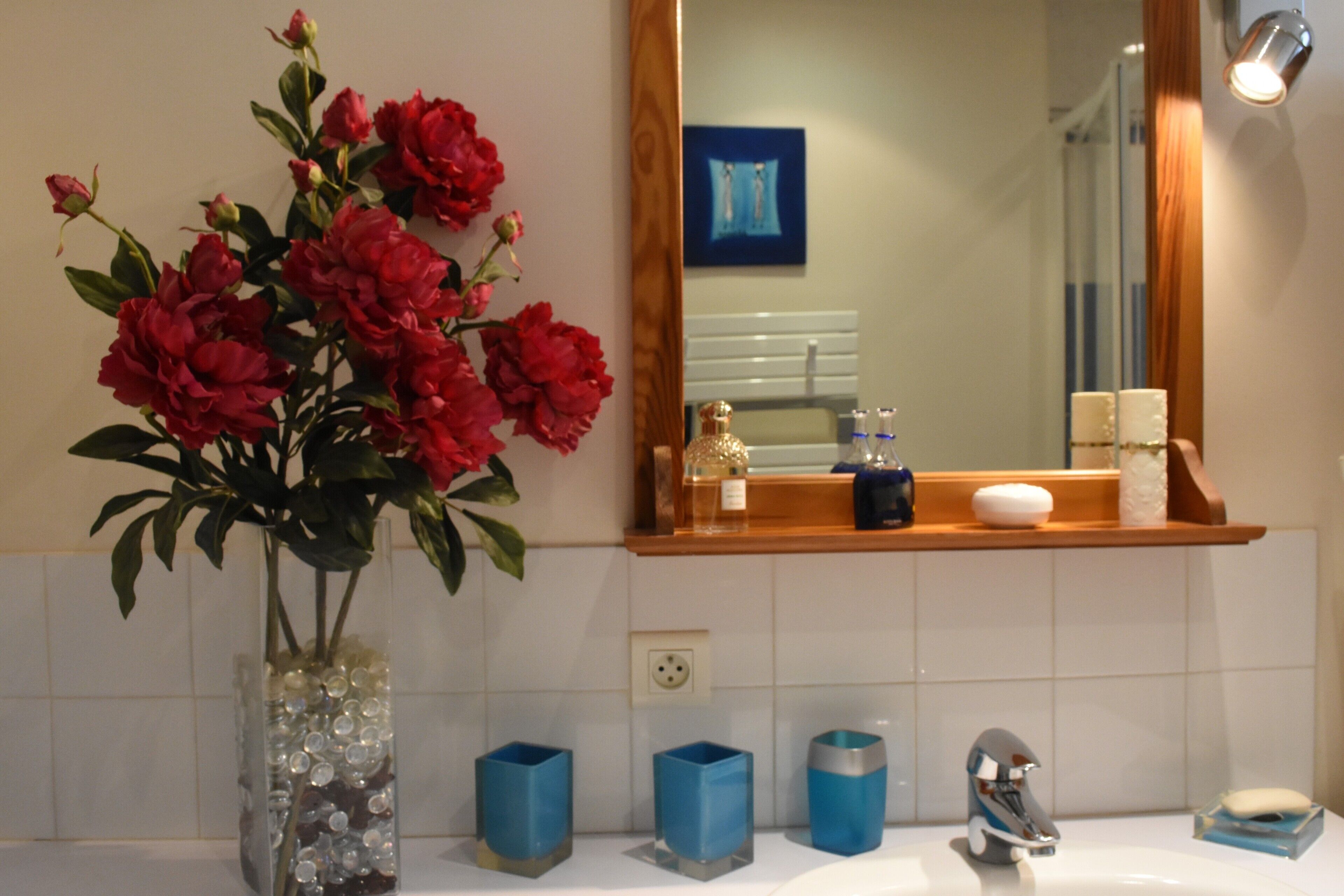 Une salle de bain avec un vase de fleurs rouges, un miroir et un lavabo doté de distributeurs de savon bleus.