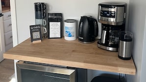 A kitchen counter with coffee-making equipment, mugs, and a QR code sign.