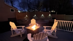 A deck with Adirondack chairs, a fire pit, and a small table.
