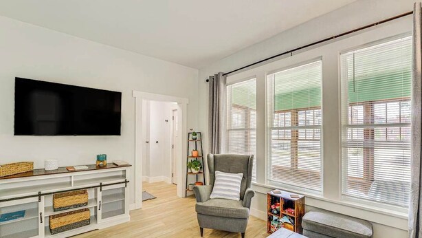 A living room with a flat-screen TV, a grey armchair, a wooden coffee table, and a bookshelf.