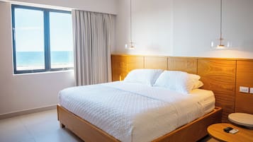 Habitación de hotel con cama, vista al mar, cabecero de madera, mesita de noche y velador.