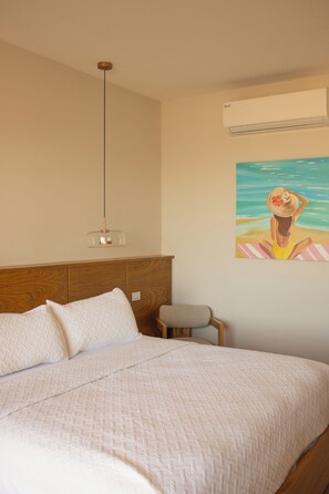 A bedroom with a bed, a wooden headboard, a hanging light fixture, a small chair, and a wall-mounted air conditioner. - Costa Elegante Hotel & Suites (Puerto Peñasco)