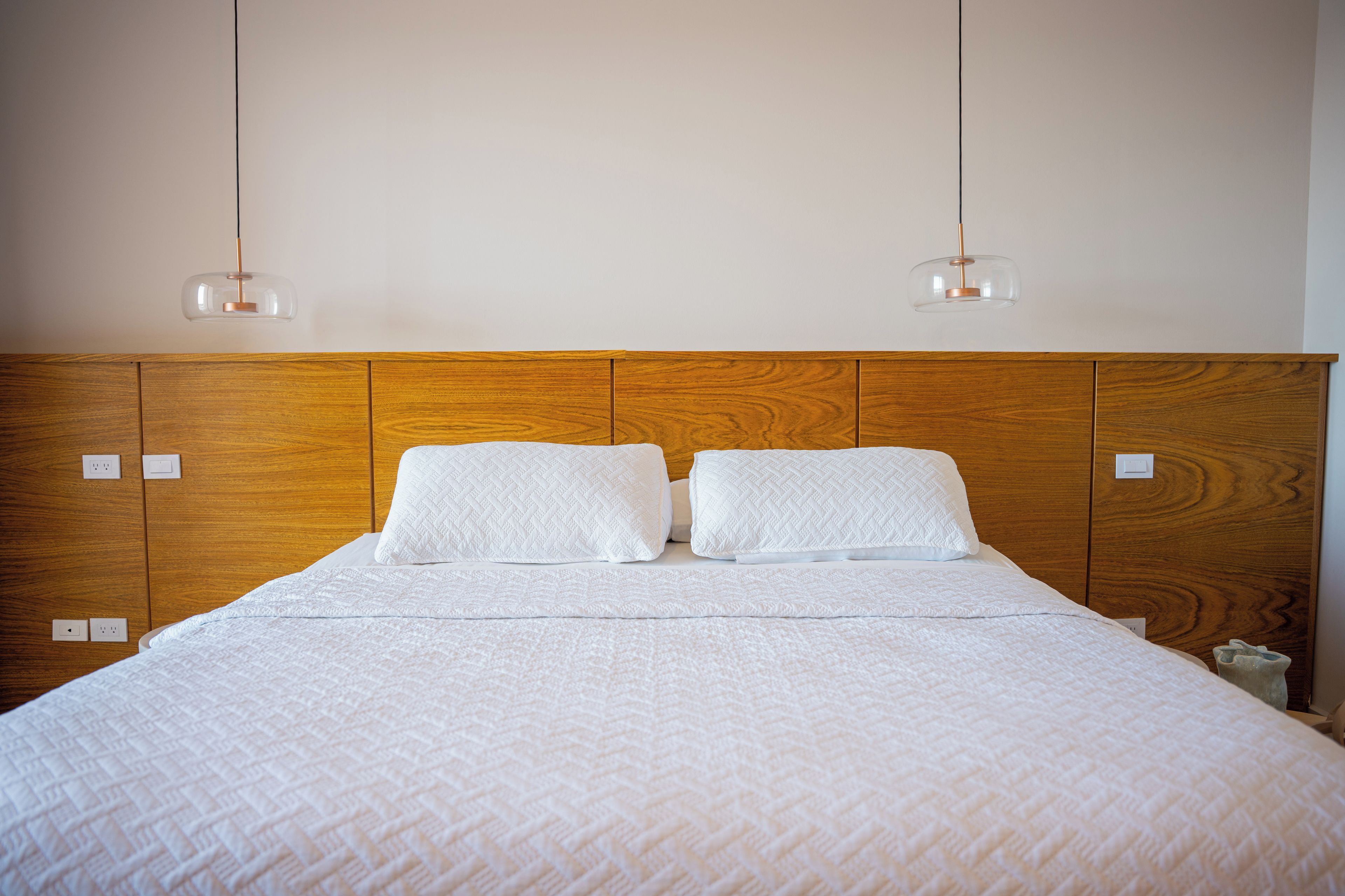 Een bed met een houten hoofdbord, twee witte kussens en een wit gebogen deken.