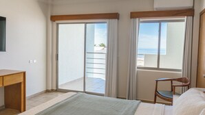 A hotel room with a bed, a desk, a chair, and a balcony with a view of the ocean.