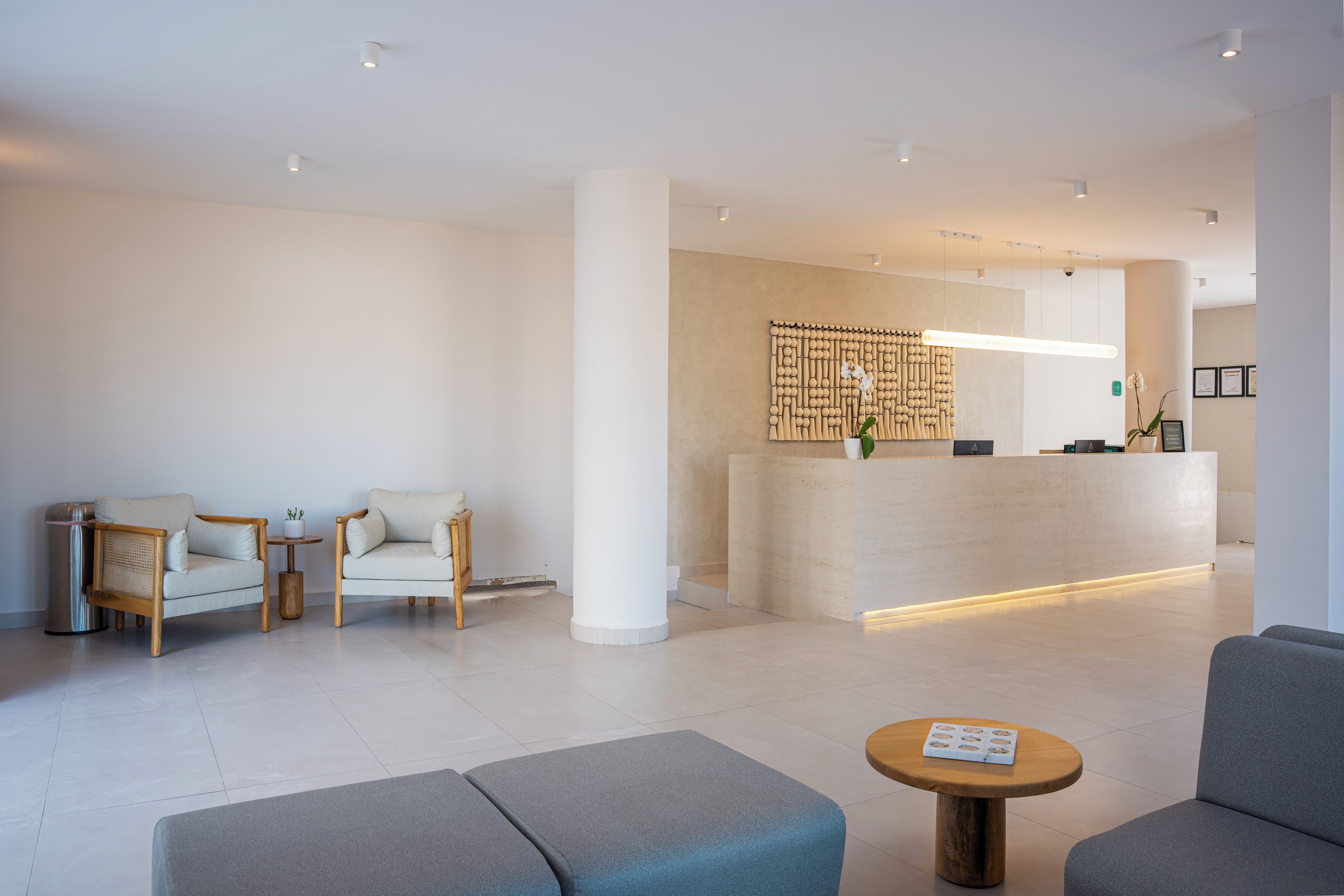 Una moderna zona de recepción con un mostrador, dos sofás, una mesa de centro y un panel decorativo en la pared.