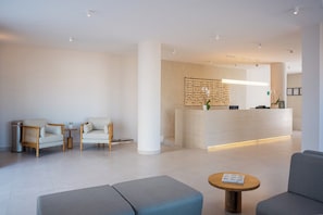 A modern reception area with a reception desk, two sofas, a coffee table, and a decorative wall panel. - Costa Elegante Hotel & Suites (Puerto Peñasco)