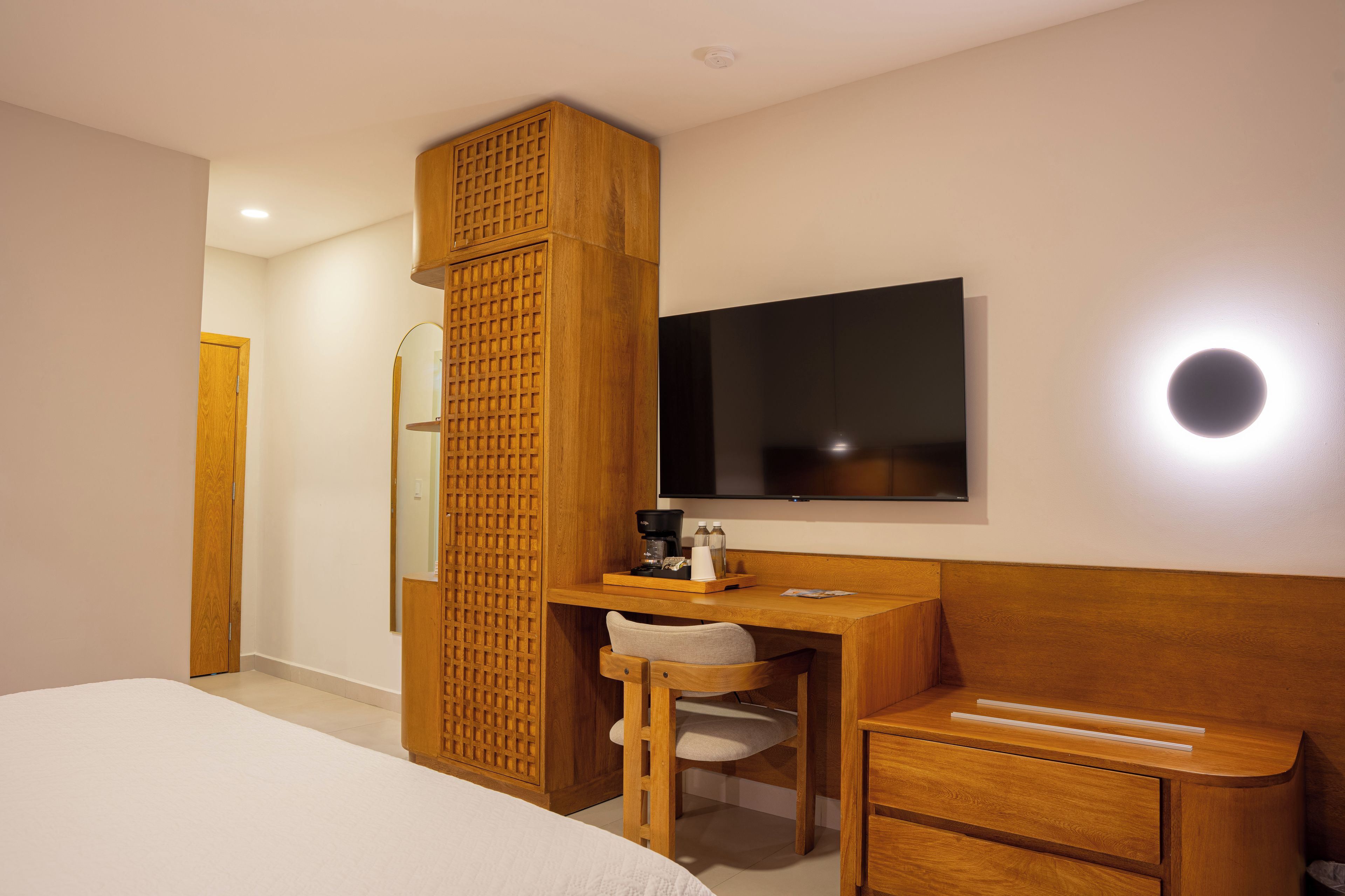 A hotel room with a bed, a desk with a chair, a television, and a wooden partition.