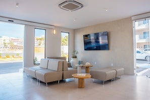 A modern hotel lobby with a large sofa set, a coffee table, and a large flat-screen TV mounted on the wall. - Costa Elegante Hotel & Suites (Puerto Peñasco)