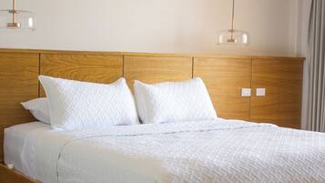 Una cama de madera con ropa de cama blanca y dos lámparas colgantes.
