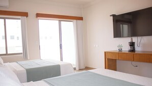 A hotel room with two beds, a wooden desk, a television, and a window with curtains.