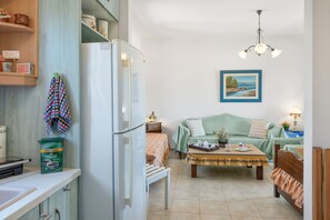 A compact living space with a kitchenette, a dining table, a sofa, and a painting on the wall.