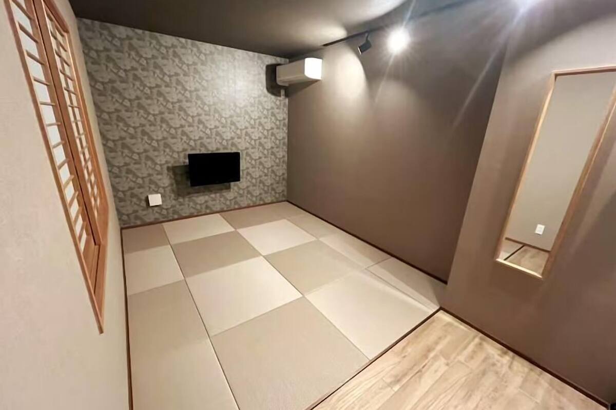 Een kamer met tatami vloerbedekking, een hangende televisie en een klein raam.