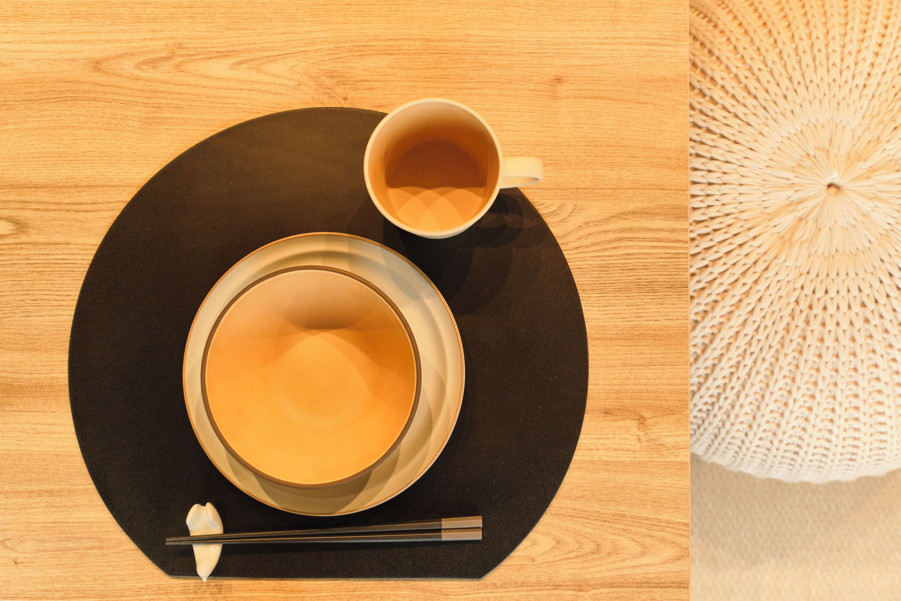 A table with a black placemat, a bowl of soup, a cup of tea, chopsticks, and a spoon.